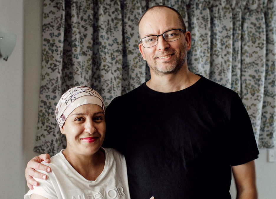 Woman wearing headscarf stands with her arms around her partner.