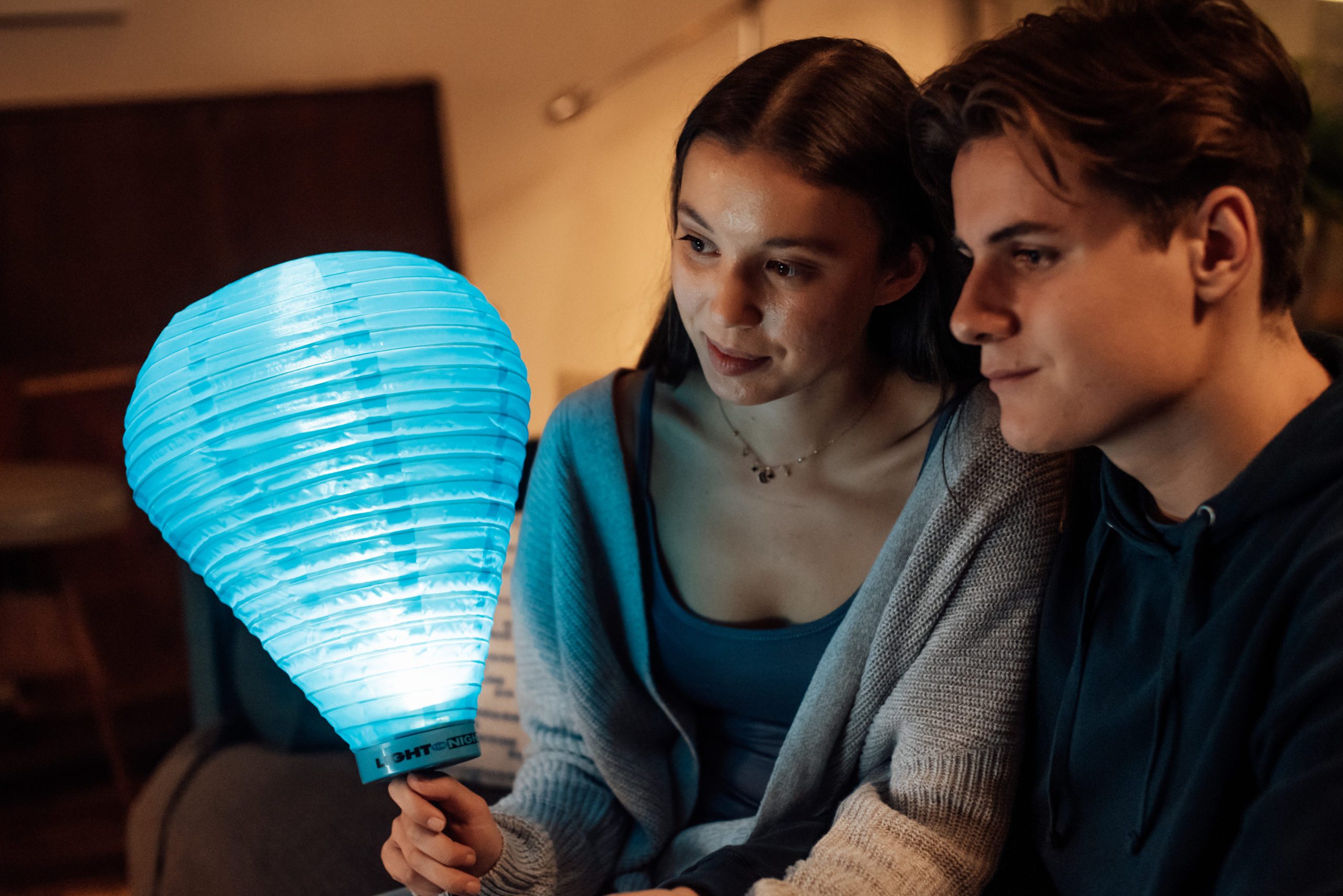 Young woman and man holding a blue Light the Night lantern in their living room