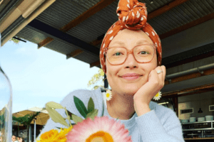 A woman wearing a head scarf sits in a cafe with flowers. She's reflecting on 100 days since her transplant.