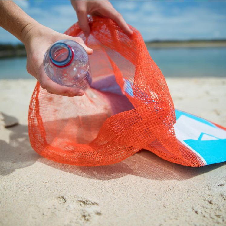 Close up of a hand putting some plastic bottles into a bag, with the beach in the background