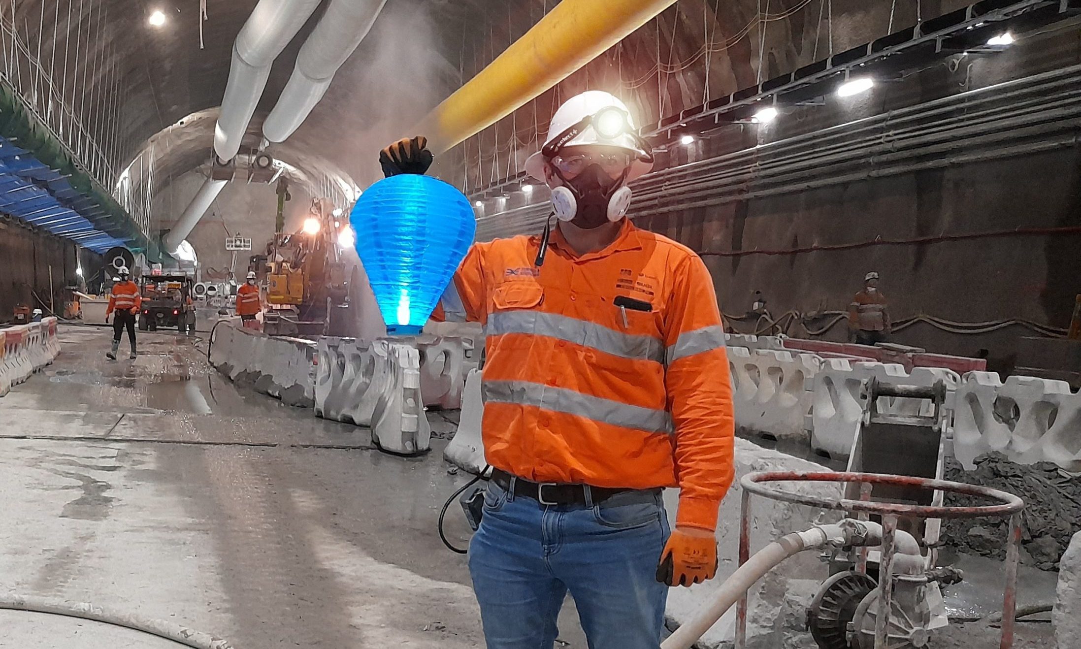 Man standing in an underground tunnel construction site, holding a Leukaemia Foundation blue Light the Night lantern