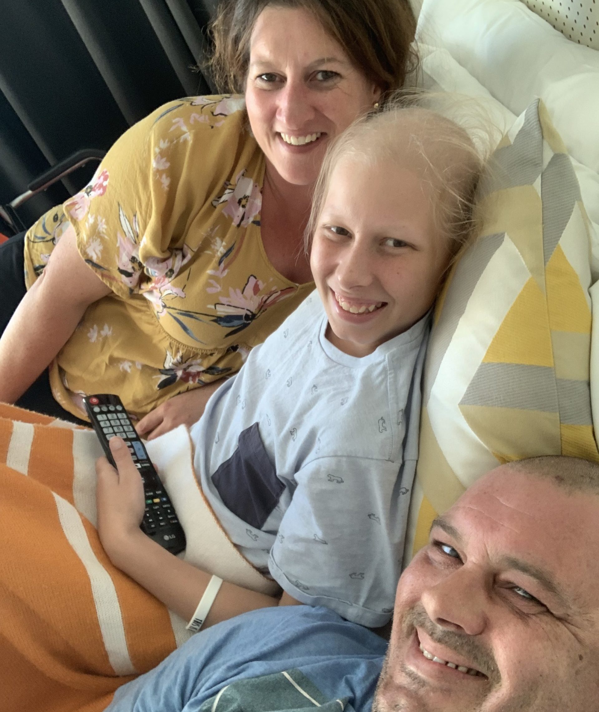 A smiling young teen boy in a hospital bed, with his parents on either side of him