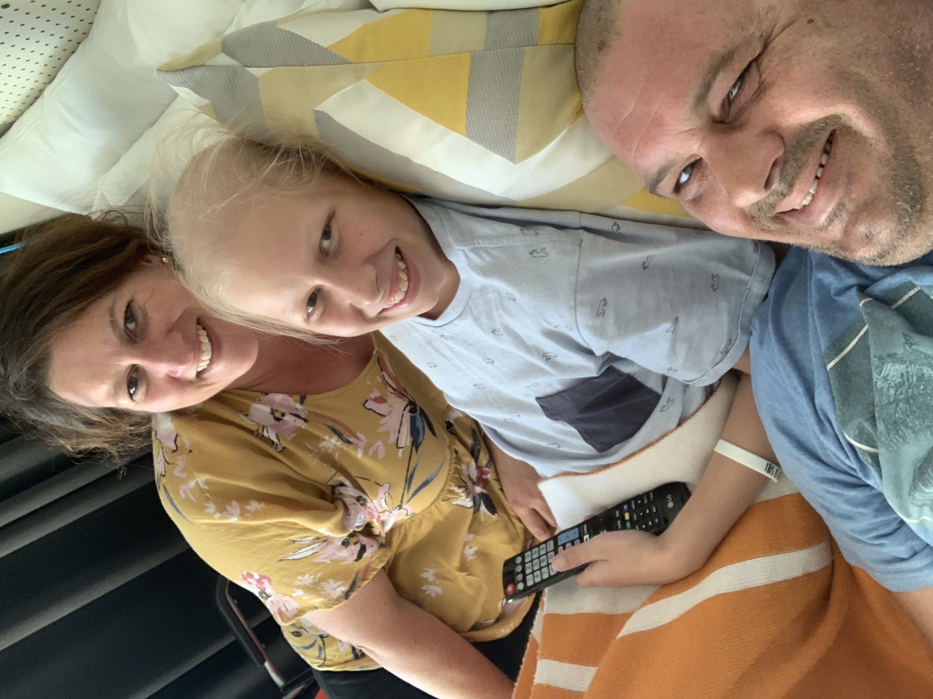A smiling young teen boy in a hospital bed, with his parents on either side of him