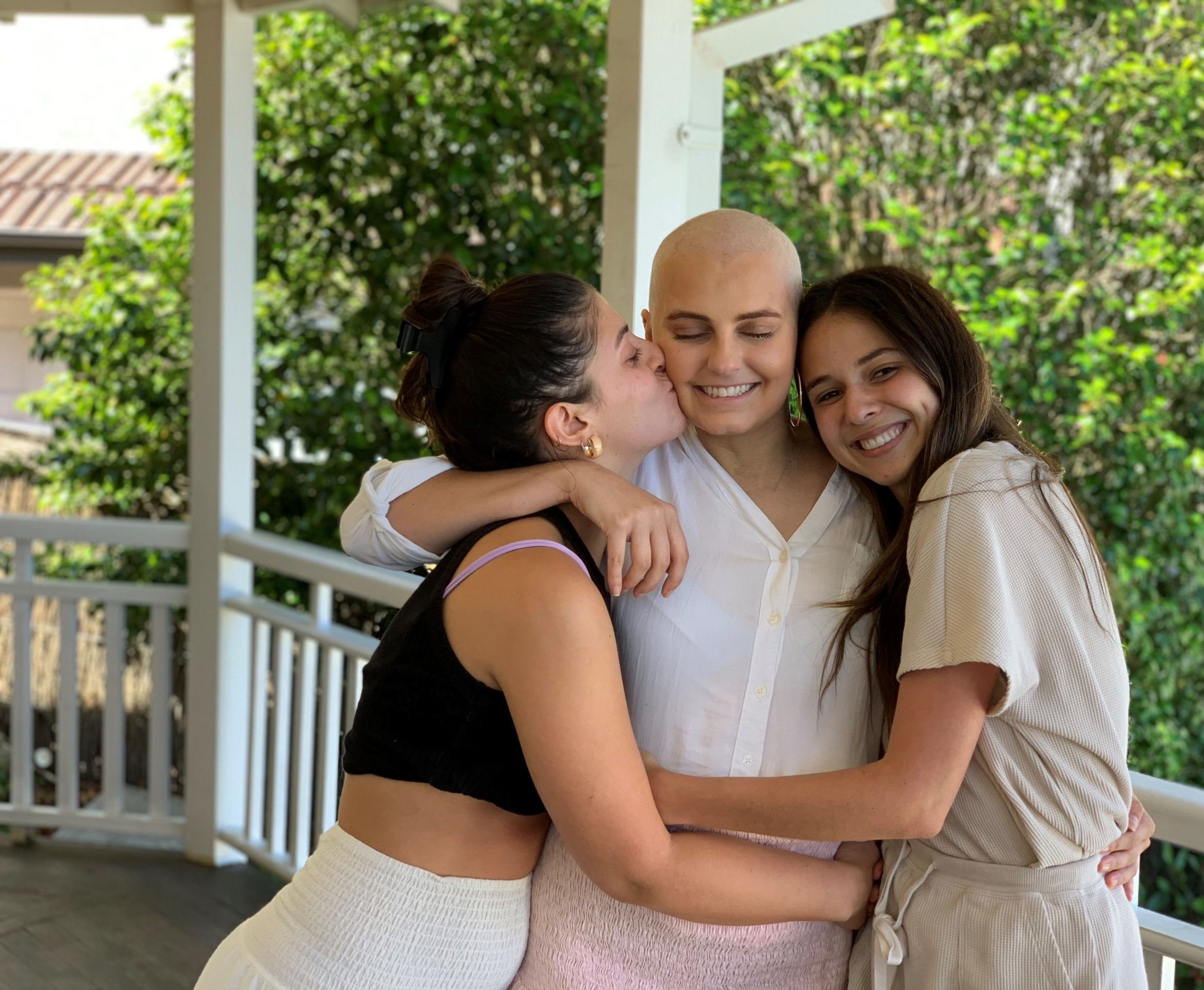 A smiling young woman being hugged by two friends