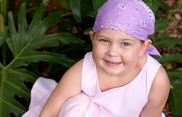 A young girl wearing a purple headscarf smiles for the camera