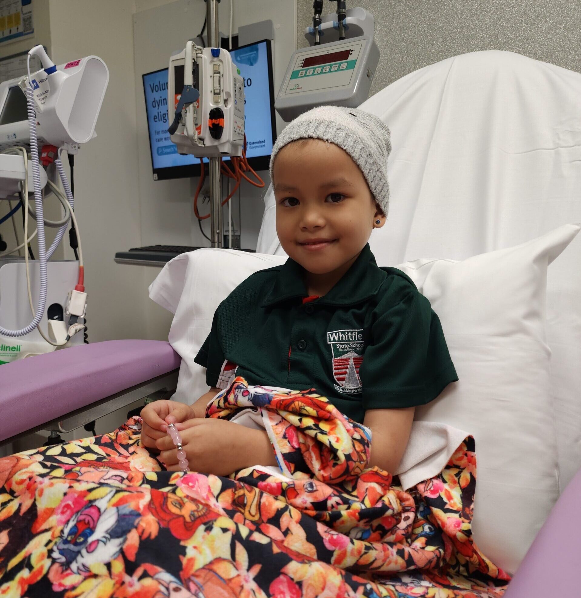 Young girl wearing a beanie sits in a hospital bed